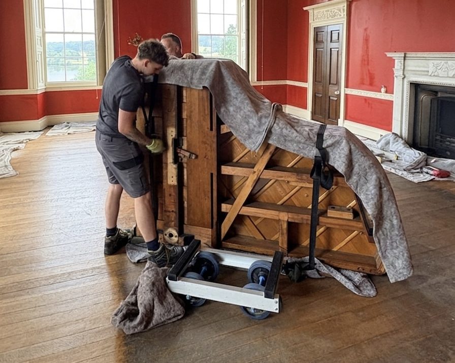 Piano Logistics Manchester movers securing a wrapped grand piano to a skid in a period drawing room