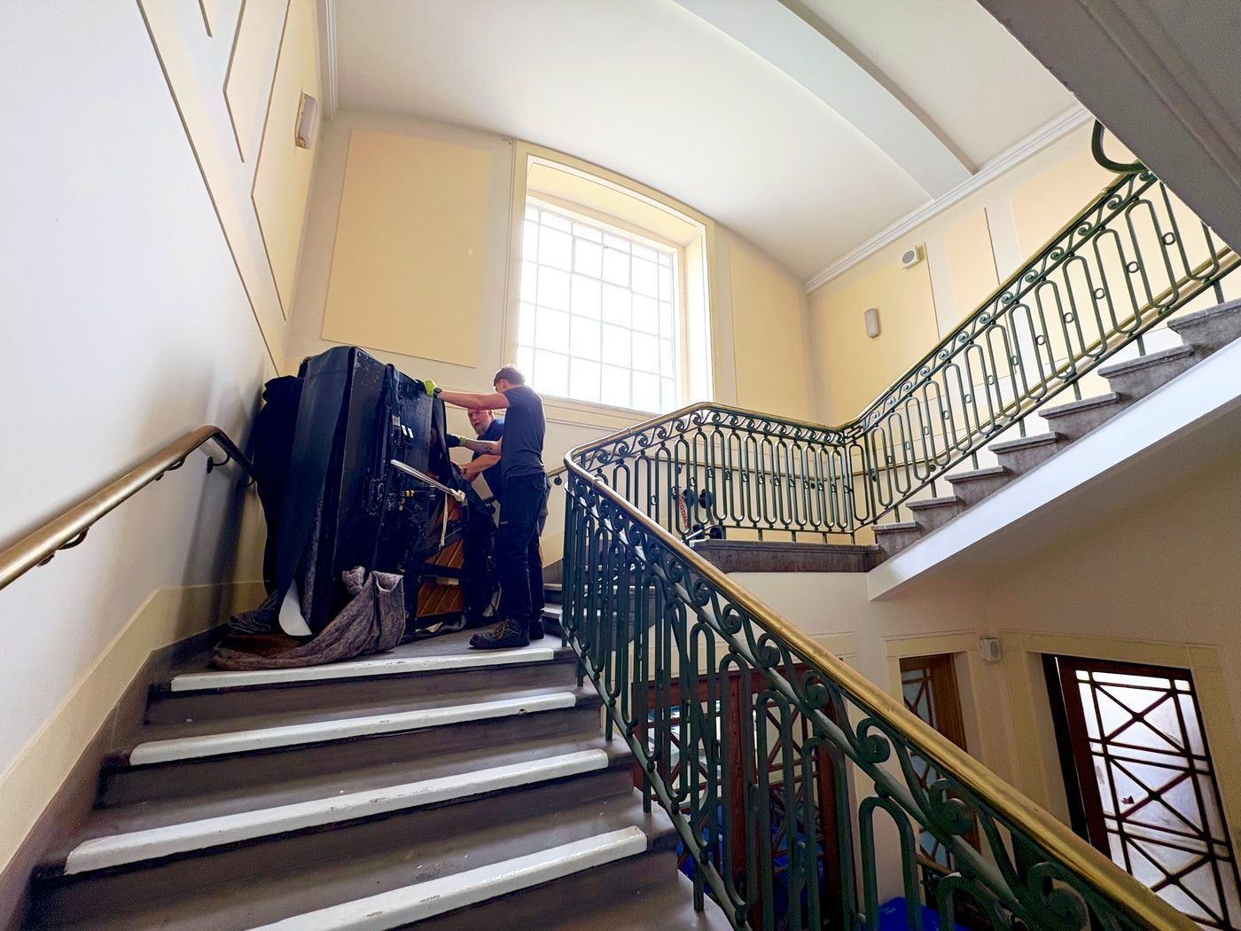 Two piano movers walking a Steinway grand piano up a flight of stairs at Wallasey Town Hall