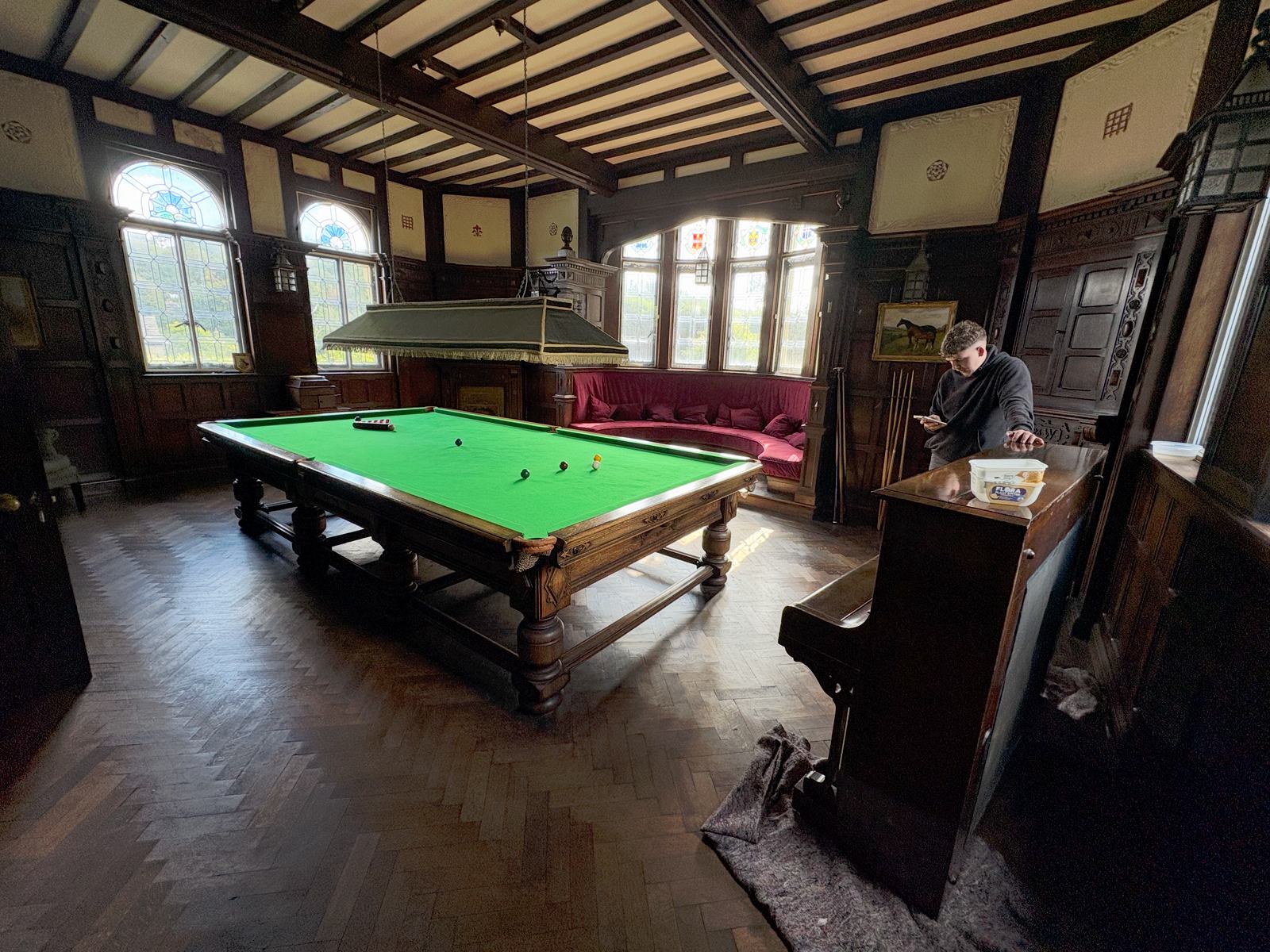 Upright piano standing on floor protection felts in an oak-panelled snooker room with a herringbone parquet floor