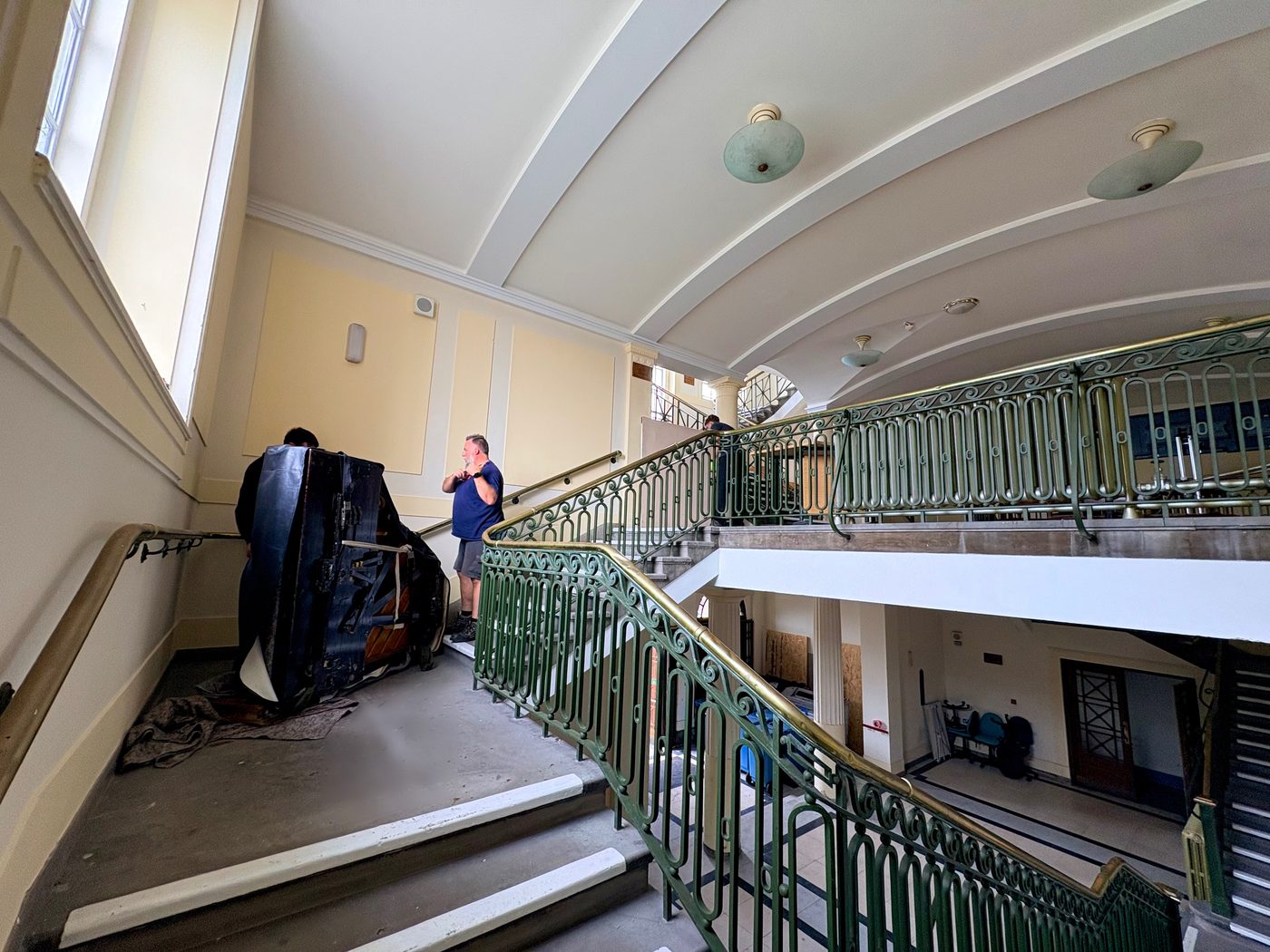 A covered grand piano on a piano board on an upper landing at Wallasey Town Hall, with the cast-iron balustrade alongside